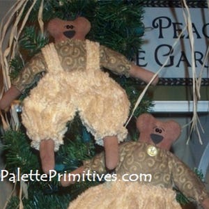 Puede incluir: Dos osos de peluche marrones con ojos marrones y narices negras llevan camisas con estampado marrón y dorado y pantalones beige. Los osos están colgados de un árbol de Navidad con un cartel que dice "Peace Garden".