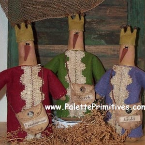 Könnte beinhalten: Drei handgefertigte Weihnachtsornamente aus Filz, die die drei Weisen aus dem Morgenland darstellen. Jede Figur trägt eine Krone und eine Robe in einer anderen Farbe. Die Weisen tragen Säcke mit den Aufschriften "Weihrauch", "Myrrhe" und "Gold". www.PalettePrimitives.com