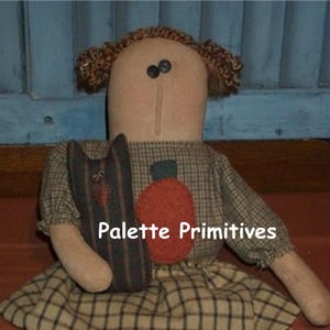 May include: A handmade rag doll with brown hair, wearing a plaid dress and holding a black cat. The doll has a pumpkin appliqué on her dress. The text "Palette Primitives" is visible in the image.