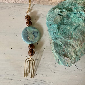 May include: A gold chain necklace with a blue and white patterned round pendant, brown wooden beads, and a gold metal arch-shaped charm.