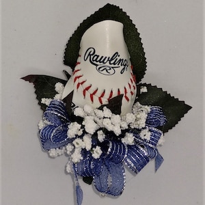 May include: A white baseball with red stitching and the Rawlings logo is arranged in a rose shape with blue and silver ribbon and white baby's breath.