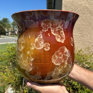 May include: A large, round, ceramic planter with a glossy finish. The planter is decorated with a pattern of white flowers on a red and orange background.