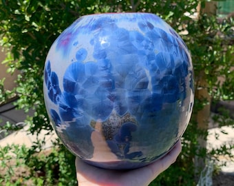 May include: A round, blue and white ceramic vase with a glossy finish. The vase has a swirling pattern of blue and white.