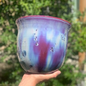 May include: A ceramic vase with a blue, purple, and white glaze. The vase has a rounded shape and a red rim.