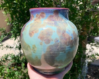 May include: A ceramic vase with a blue, green, and purple iridescent glaze. The vase has a round body and a wide opening.