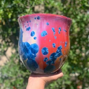 May include: A red and white ceramic planter with blue and white speckles. The planter is in the shape of a vase and has a wide mouth.