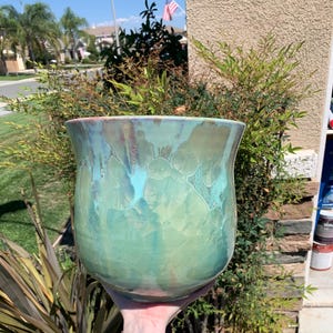 May include: A large, green ceramic planter with a unique, marbled glaze. The glaze has a light blue and green color with a hint of pink.