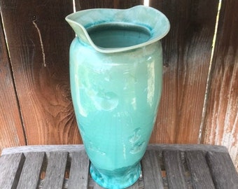 May include: A turquoise ceramic vase with a wide, flared opening and a slightly rounded base. The vase has a textured, mottled surface.