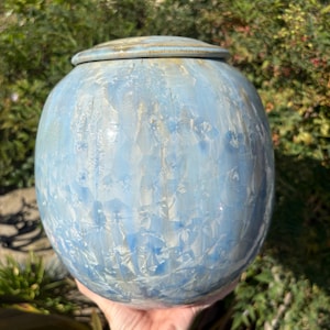 May include: A round ceramic vessel with a lid, featuring a glossy crystalline glaze in shades of light blue and white. The surface displays a distinctive starburst pattern created by the crystallization process, with a smooth, rounded silhouette.