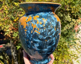 May include: A ceramic vase with a unique crystalline glaze. The vase features a dark blue and orange color scheme. The glaze has a textured, almost fractal-like pattern. The vase has a wide mouth and a rounded body, suitable for displaying flowers or as a decorative piece.