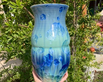 May include: A blue and green ceramic vase with a floral design. The vase has a rounded body and a narrow neck.