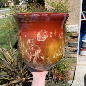 May include: A large, red and gold ceramic planter with a unique, white, speckled glaze. The planter has a wide, round base and a slightly narrower opening.
