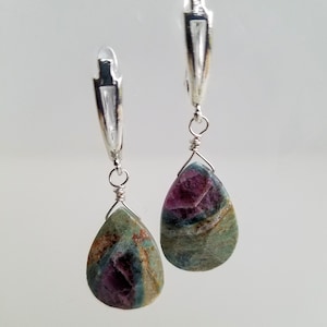 May include: A pair of silver hoop earrings with teardrop-shaped green and pink gemstone pendants.