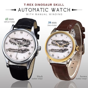 May include: Two automatic watches with manual winding. One has a 42 mm silver tone case and black leather straps. The other has a 38 mm two-tone case and brown leather straps. Both watches feature a T-Rex dinosaur skull design on the face.