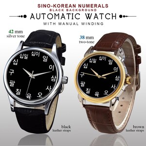 May include: Two automatic watches with black faces and Sino-Korean numerals. One watch has a silver tone case and a black leather strap, measuring 42 mm. The other has a two-tone case and a brown leather strap, measuring 38 mm.