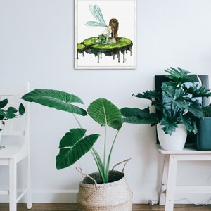 May include: A watercolor painting of a fairy with green wings sitting on a green lily pad. The lily pad is dripping with water. The painting is framed in a white frame.
