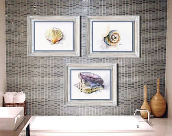Pode incluir: Três pinturas de aquarela emolduradas de conchas. A pintura superior esquerda apresenta uma concha branca com um interior amarelo e laranja. A pintura superior direita apresenta uma concha marrom com um interior amarelo e laranja. A pintura inferior apresenta uma concha roxa e branca.
