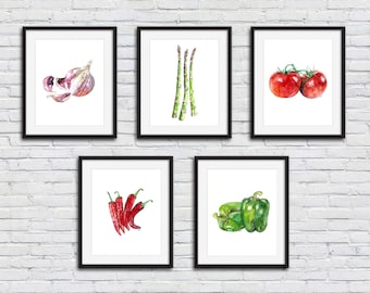 May include: Five framed watercolor paintings of various vegetables and herbs. The paintings are arranged in a row on a white brick wall. The paintings include a garlic bulb, a bunch of asparagus, two red tomatoes, a bunch of red chili peppers, and two green bell peppers.