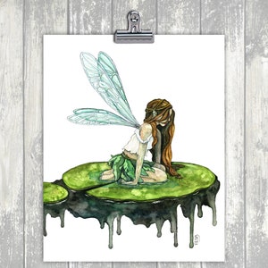 May include: Watercolor painting of a fairy with green wings sitting on a green lily pad with dripping black edges. The fairy has long brown hair and is wearing a white top and green skirt.