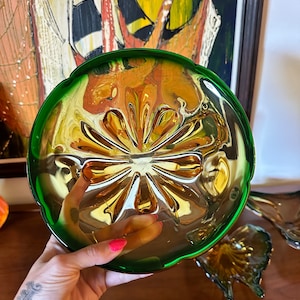 May include: A vintage amber glass serving dish with a green rim. The dish has a scalloped edge and a floral design on the bottom.