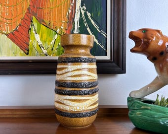 May include: A brown and white ceramic vase with black stripes. The vase has a textured surface and a rounded shape.