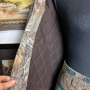 Puede incluir: Una chaqueta de camuflaje con forro acolchado marr&oacute;n y un pantal&oacute;n de camuflaje a juego. La chaqueta tiene cierre de cremallera y cuello acanalado marr&oacute;n. El estampado de camuflaje presenta tonos de marr&oacute;n, verde y beige.