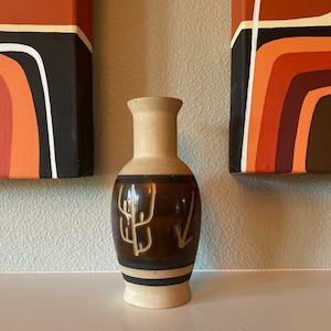 May include: A brown and beige ceramic vase with a geometric design. The vase has a narrow neck and a wide base. It is decorated with a stylized tree and arrow design.