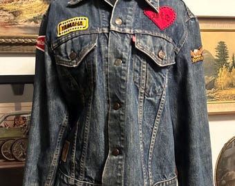May include: A blue denim jacket with patches, including a red heart with "Wife" embroidered on it, a yellow "Yamaha" patch, and a brown eagle patch.