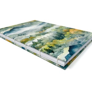 May include: A watercolour-patterned journal with a blue, green and yellow design. The journal is bound with white stitching and has a white spine.