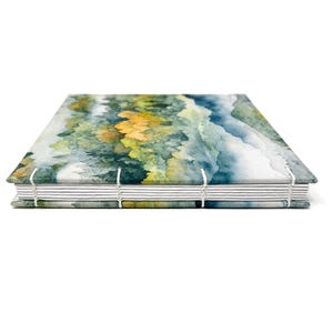 May include: A watercolor landscape journal with a blue, green, and yellow design. The journal is bound with white thread and has a white spine.