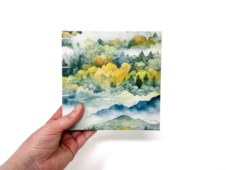 May include: A watercolor painting of a misty forest scene with green and yellow trees and blue mountains in the background.
