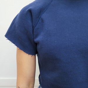 May include: A navy blue cropped sweatshirt with a crew neck and raglan sleeves. The sweatshirt has a distressed hem.