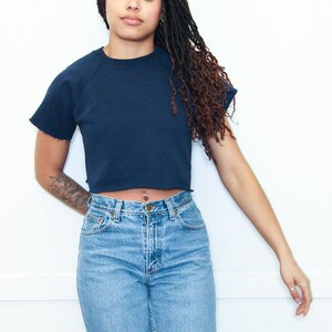 May include: A woman wearing a navy blue cropped t-shirt with a raw hem and light blue jeans.