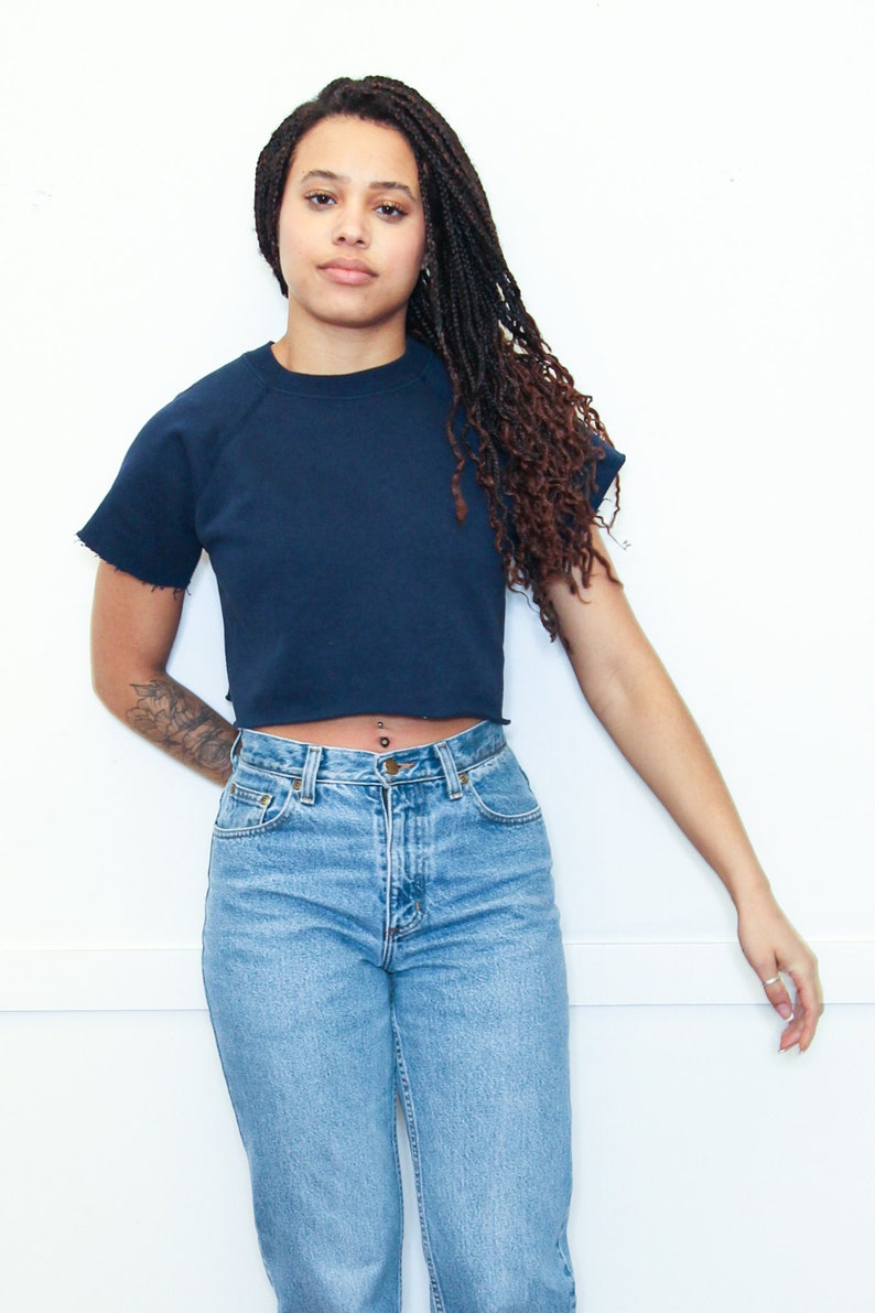 May include: A woman wearing a navy blue cropped t-shirt with a raw hem and light blue jeans.