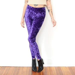 May include: High-waisted leggings in a deep purple crushed velvet fabric. These fitted trousers feature a full-length design that tapers down to the ankles, showcasing a distinct textured sheen characteristic of crushed velvet material throughout.