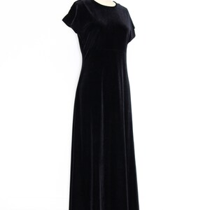 Puede incluir: Un vestido maxi de terciopelo negro con mangas cortas y cuello redondo. El vestido est&aacute; sobre un fondo blanco.