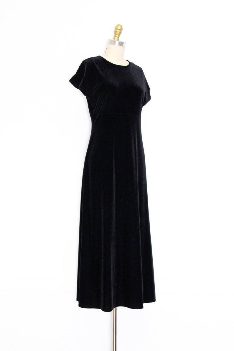 Puede incluir: Un vestido maxi de terciopelo negro con mangas cortas y cuello redondo. El vestido est&aacute; sobre un fondo blanco.