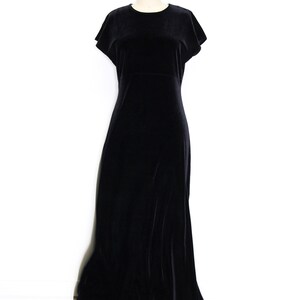 Puede incluir: Un vestido maxi de terciopelo negro con mangas cortas y cuello redondo. El vestido est&aacute; sobre un fondo blanco.