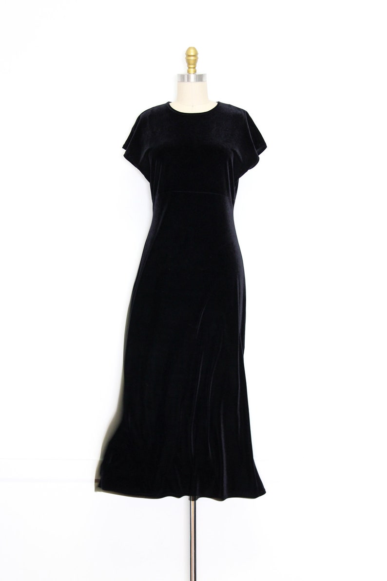 Puede incluir: Un vestido maxi de terciopelo negro con mangas cortas y cuello redondo. El vestido est&aacute; sobre un fondo blanco.