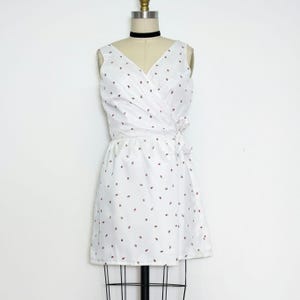 Könnte beinhalten: Ein weißes Wickelkleid mit einem kleinen roten und blauen Blumenmuster. Das Kleid hat einen V-Ausschnitt und ist ärmellos.