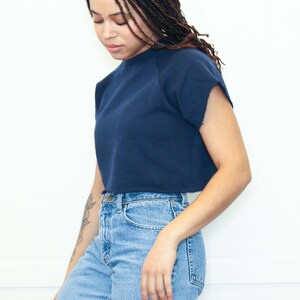 May include: A woman wearing a navy blue cropped sweatshirt with short sleeves and light blue jeans.