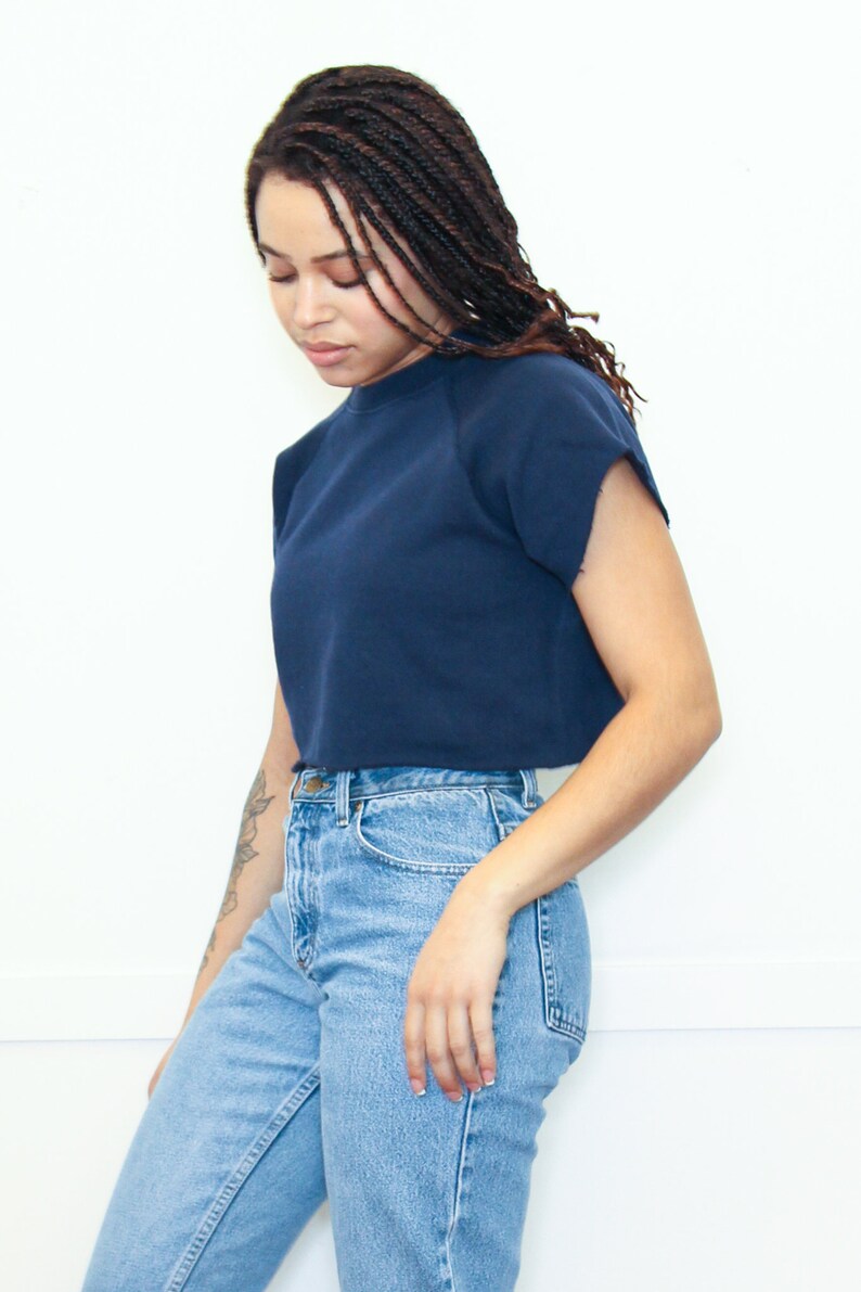 May include: A woman wearing a navy blue cropped sweatshirt with short sleeves and light blue jeans.