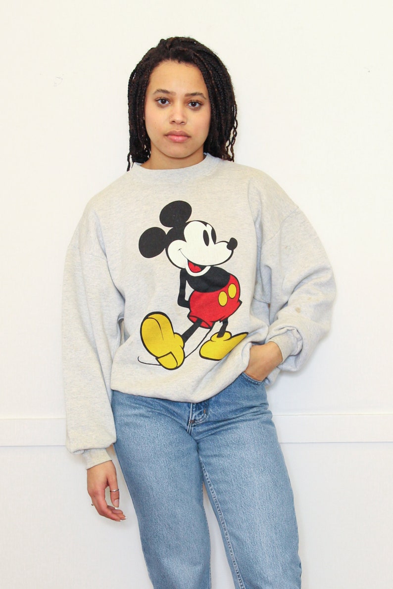 May include: A gray sweatshirt with a vintage Mickey Mouse graphic. The sweatshirt has long sleeves and a crew neck.