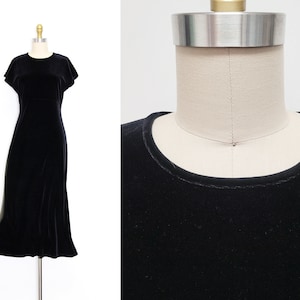 Puede incluir: Un vestido de terciopelo negro con cuello redondo y mangas cortas. El vestido est&aacute; ajustado en el corpi&ntilde;o y fluye hacia afuera hasta una longitud midi.