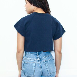 May include: A navy blue cropped sweatshirt with short sleeves and a relaxed fit. The sweatshirt is worn with light blue denim jeans.