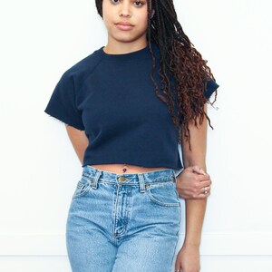 May include: A woman wearing a navy blue cropped sweatshirt with a high neckline and a pair of light blue denim jeans.