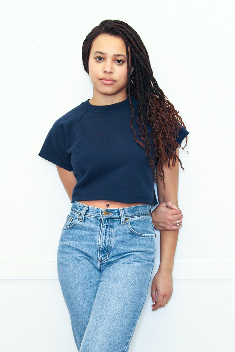 May include: A woman wearing a navy blue cropped sweatshirt with a high neckline and a pair of light blue denim jeans.
