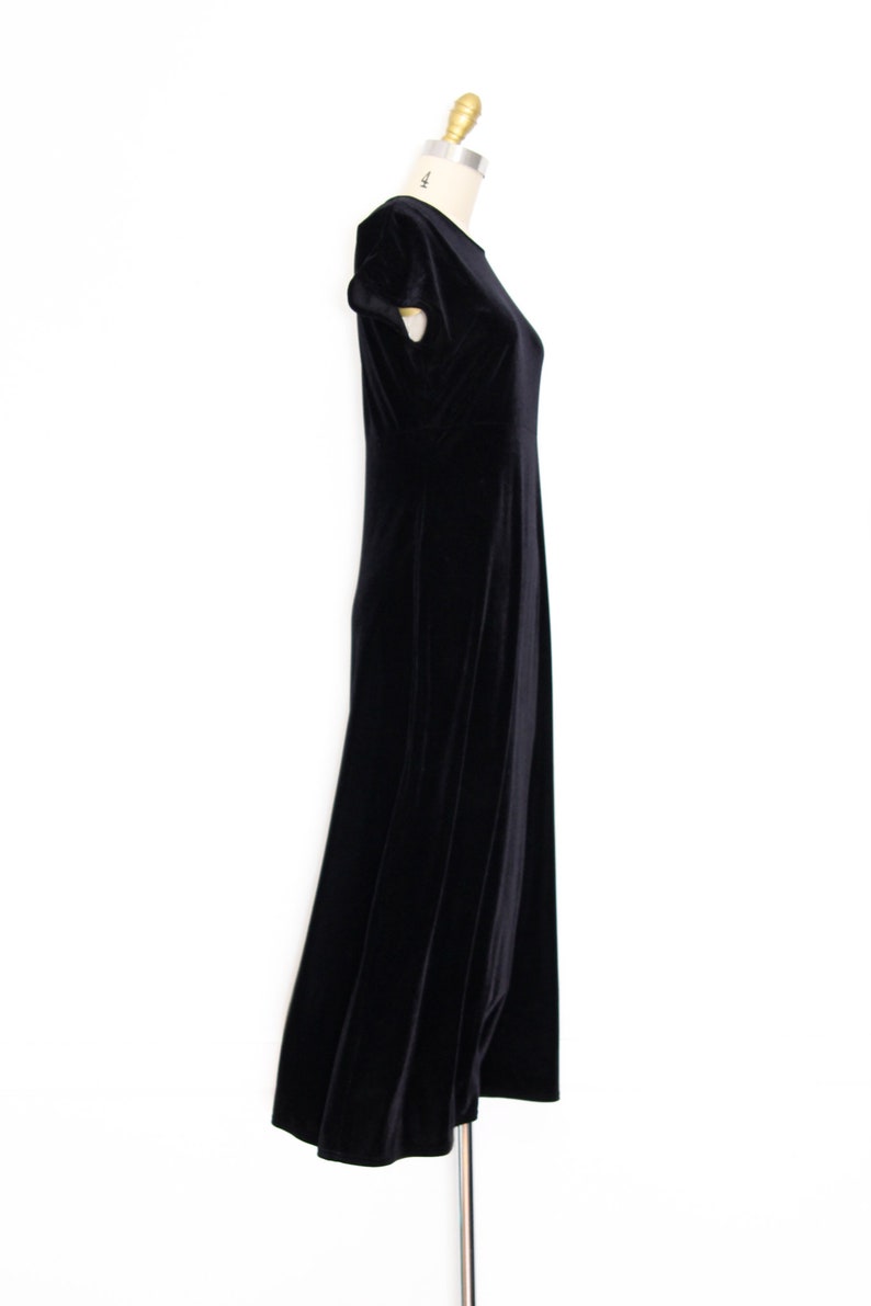 Puede incluir: Un vestido maxi de terciopelo negro con mangas cortas. El vestido est&aacute; sobre un fondo blanco.