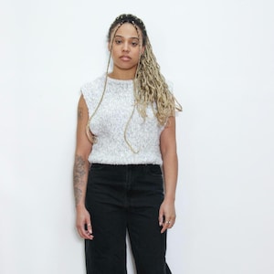 May include: A woman wearing a white knit sleeveless top with a round neckline and black jeans.