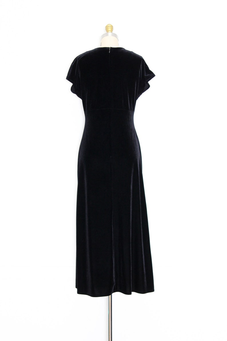 Puede incluir: Un vestido maxi de terciopelo negro con mangas cortas y escote en V. El vestido tiene un corpi&ntilde;o ajustado y una falda fluida.